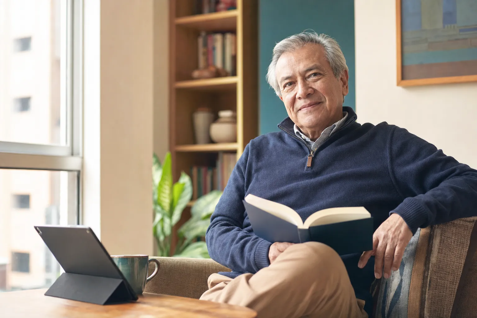 Hombre mayor leyendo en casa, con una tableta a su lado